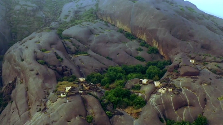 قرية غيه في منطقة عسير، لقطة جوية تُظهر المنازل فوق الصخور والأشجار.