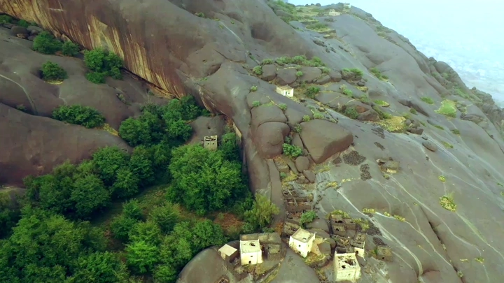 قرية غيه في منطقة عسير، لقطة جوية تُظهر المنازل فوق الصخور والأشجار.