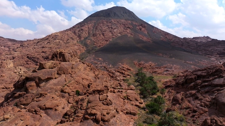 قمة جبلية بأعمدة بازلتية وصخور ملونة في حائل، لقطة جوية.