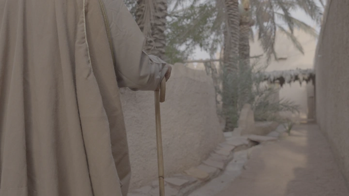 رجل مسن يمشي في ممر بيت طيني، لقطة خلفية.