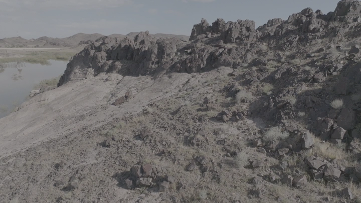 جبل صخري في حائل بعد المطر خلفه واحة خضراء، لقطة جوية.