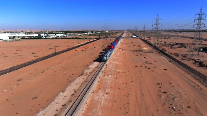 قطار شحن طويل يسير في الصحراء تحت أشعة الشمس، لقطة جوية.