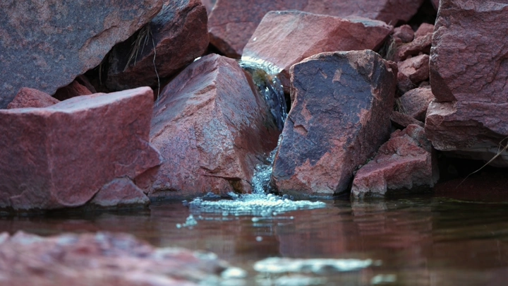 شلال صغير من الأمطار يتدفق بين الصخور، لقطة قريبة.