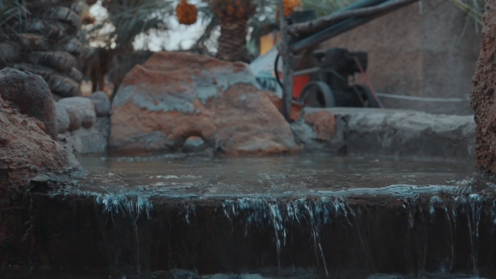 مياه تتدفق في مزرعة مع نخيل في الخلفية، لقطة قريبة.