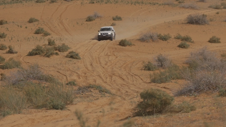 سيارة تسير في صحراء حائل خلال رالي، لقطة بعيدة.