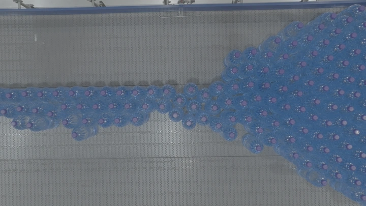 زجاجات مياه بلاستيكية على خط إنتاج في مصنع، لقطة علوية.