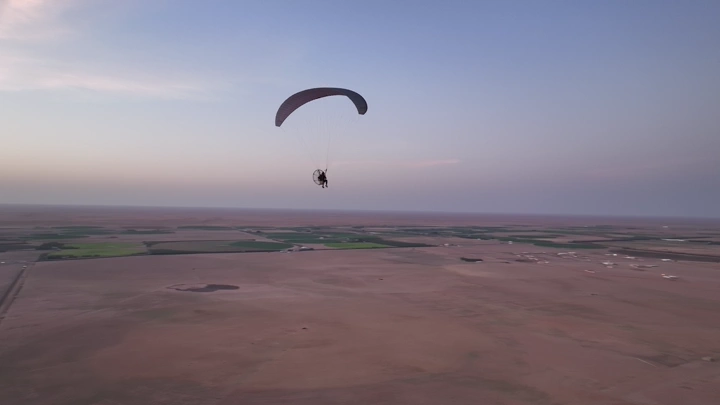 مظلي يحلق فوق الأراضي الزراعية عند الغروب، لقطة جوية.