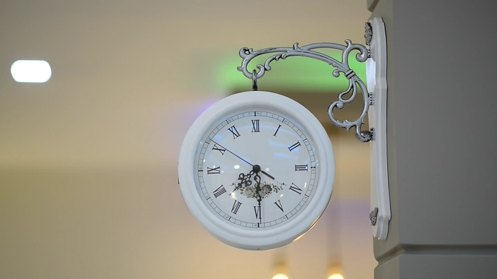 ساعة حائط بيضاء معلقة على جدار داخلي، لقطة قريبة.