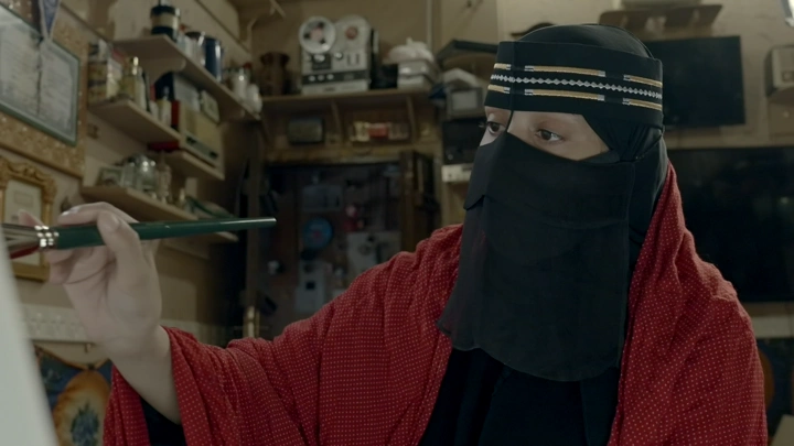 فتاة في لبس تقليدي ترسم في بيت طيني، لقطة داخلية.