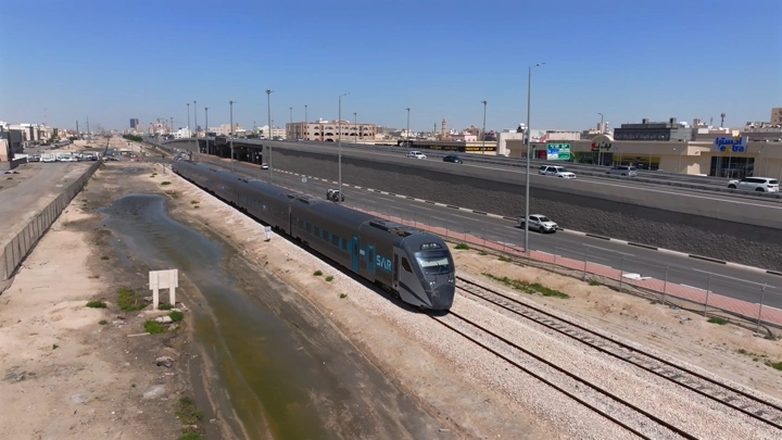 قطار يسير بجانب طريق سريع في يوم مشمس، لقطة جوية.