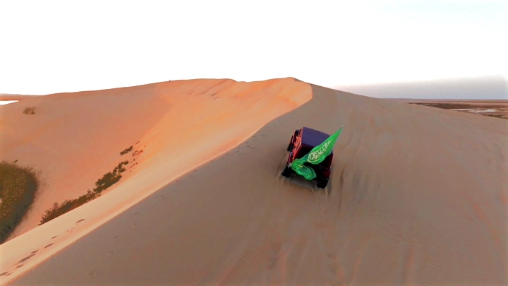 سيارة تسير على كثبان رملية تحمل علم السعودية في بحيرة الأصفر في الأحساء، لقطة جوية.