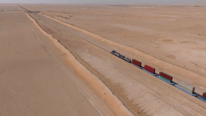 قطار شحن يسير في الصحراء خلال النهار، لقطة جوية.