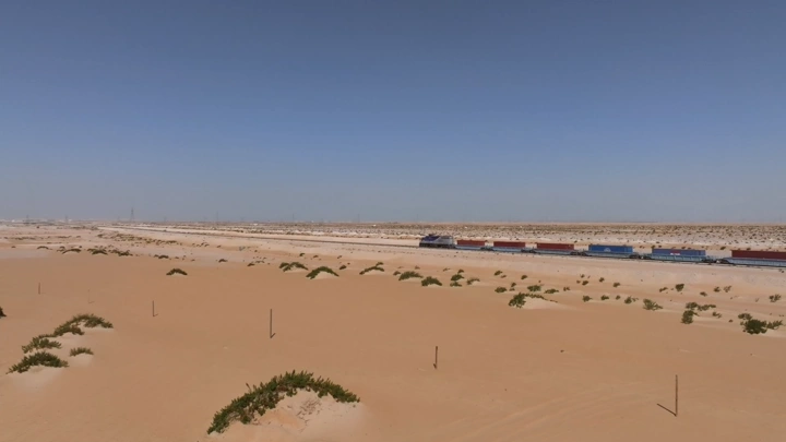 قطار شحن يعبر الصحراء تحت سماء زرقاء، لقطة جوية.