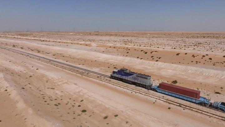 قطار شحن يسير في صحراء شاسعة تحت سماء زرقاء، لقطة جوية.