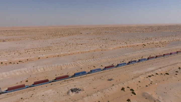 قطار شحن طويل في الصحراء تحت سماء زرقاء، لقطة جوية.