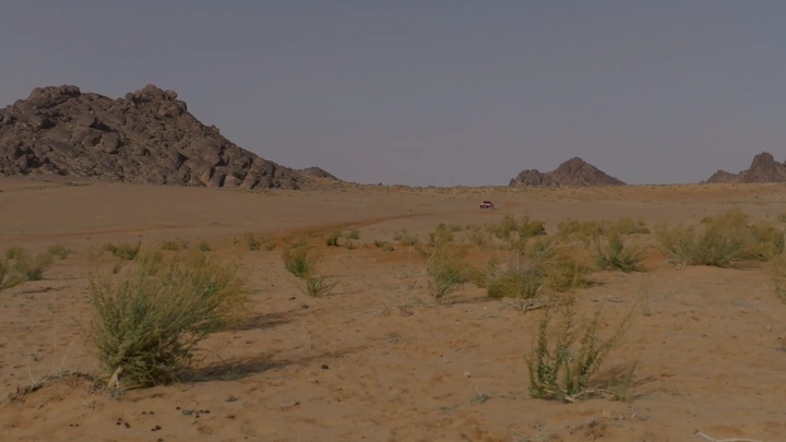 صحراء مع جبال وسيارة رالي في حائل، لقطة بعيدة.