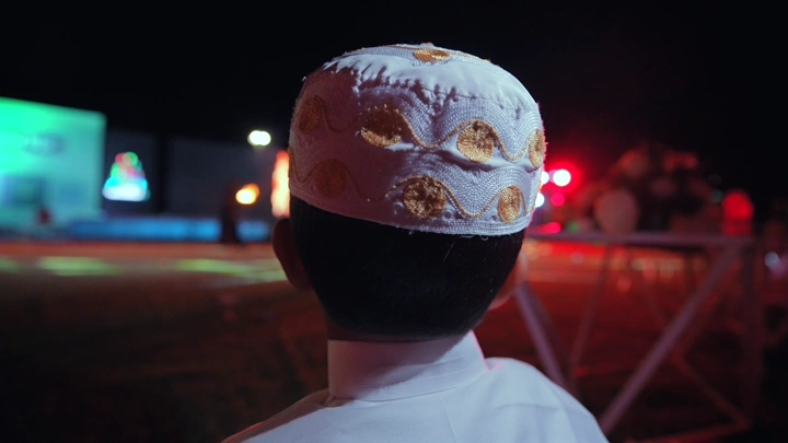 طفل يرتدي طاقية يشاهد عرض ألعاب نارية في المسرح، لقطة ليلية.