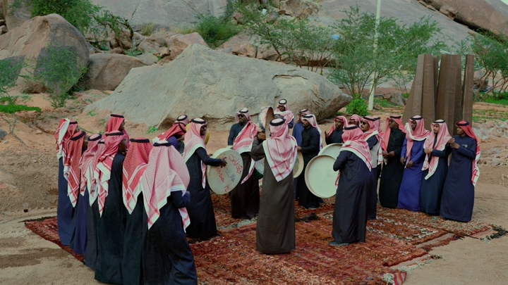 مجموعة رجال يرتدون الزي التقليدي يؤدون رقصة العرضة في الهواء الطلق.