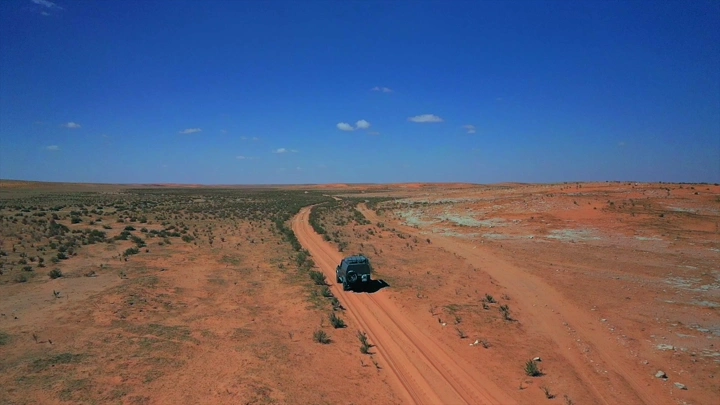 سيارة تسير في صحراء شاسعة تحت سماء زرقاء، لقطة جوية.