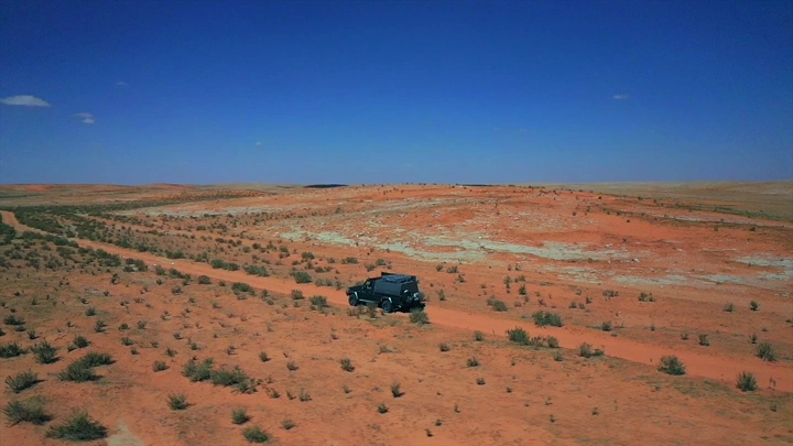 سيارة دفع رباعي في صحراء شاسعة تحت سماء زرقاء، لقطة جوية.
