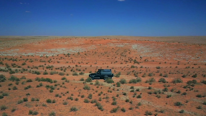 سيارة دفع رباعي في صحراء برية تحت سماء زرقاء، لقطة جوية.