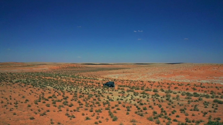 سيارة في صحراء النفود تحت سماء زرقاء، لقطة جوية.