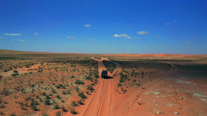 سيارة تسير في صحراء شاسعة تحت سماء زرقاء، لقطة جوية.