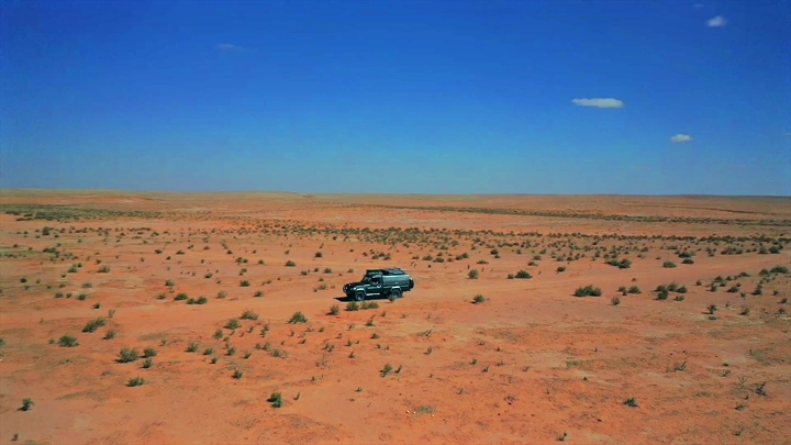 سيارة في صحراء شاسعة تحت سماء زرقاء، لقطة جوية.