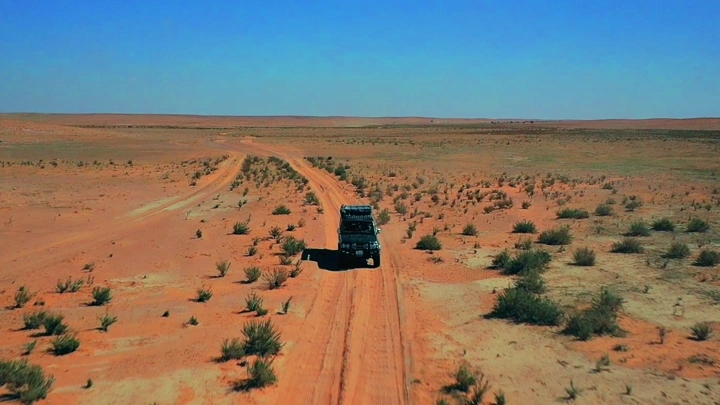 سيارة تسير في صحراء شاسعة تحت سماء زرقاء، لقطة جوية.