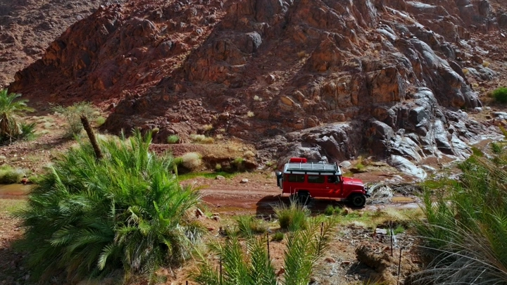 جيب أحمر يسير في الجبال الصخرية، لقطة نهارية.