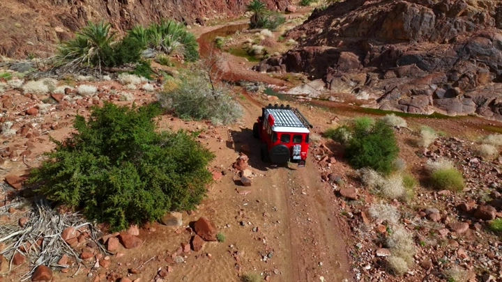 A classic red Jeep driving on a mountain road, aerial shot.