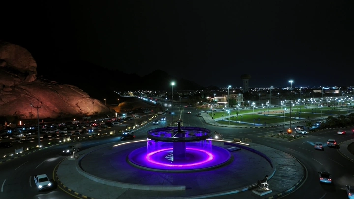 دوار مضاء بألوان بنفسجية في مدينة حائل ليلاً، منظر جوي.