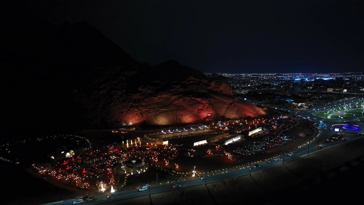 مشهد ليلي لجبال مضيئة في حائل مع المدينة في الخلفية، تصوير جوي.