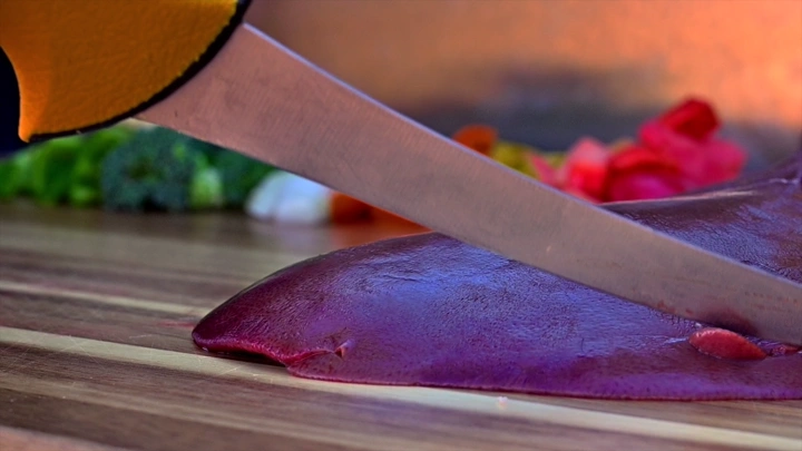 سكين تقطع قطعة لحم على لوح تقطيع خشبي، لقطة مقربة.