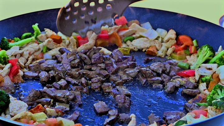 طهي لحم وخضروات في مقلاة كبيرة، لقطة مقربة.