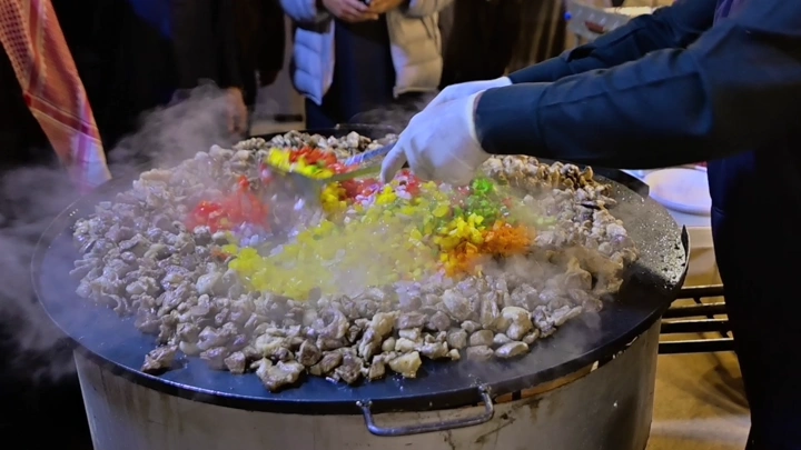 طهي لحم وخضار على صاج كبير في الهواء الطلق، لقطة ليلية.