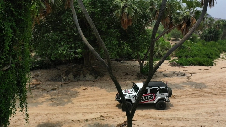 سيارة دفع رباعي تسير في طريق رملي بين الأشجار، لقطة من الأعلى.