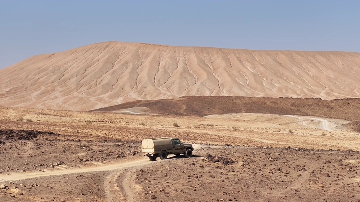 سيارة دفع رباعي في صحراء جبلية تحت سماء صافية، لقطة من الأرض.