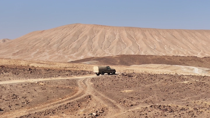 سيارة في صحراء السعودية تحت سماء زرقاء، لقطة نهارية.