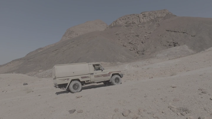 سيارة دفع رباعي في صحراء جبلية بالسعودية، لقطة جانبية.