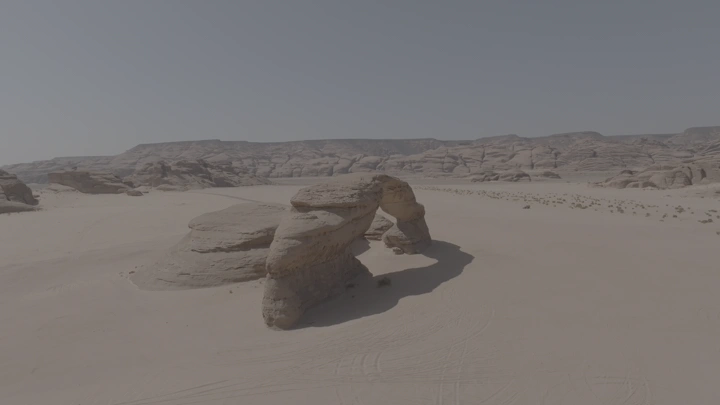 قوس صخري في صحراء واسعة تحت سماء صافية، لقطة جوية.