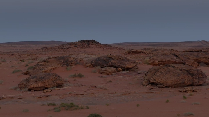 صخور كبيرة في صحراء شاسعة عند الغروب، منظر طبيعي.