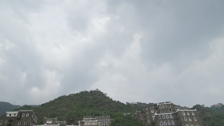 مباني تقليدية على تلال خضراء تحت سماء غائمة، لقطة واسعة.