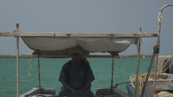 صياد يجلس في قارب تحت مظلة في البحر، لقطة نهارية.