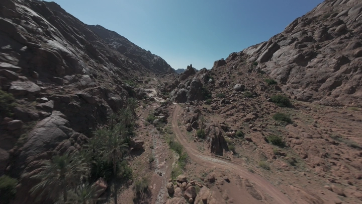 هايكينج ممر جبلي في وادٍ صخري تحت سماء زرقاء، لقطة جوية.