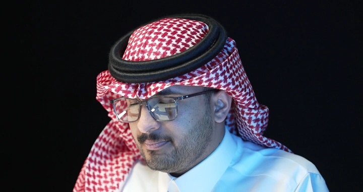 رجل يرتدي نظارات وغترة يعمل في مكتب، لقطة قريبة.