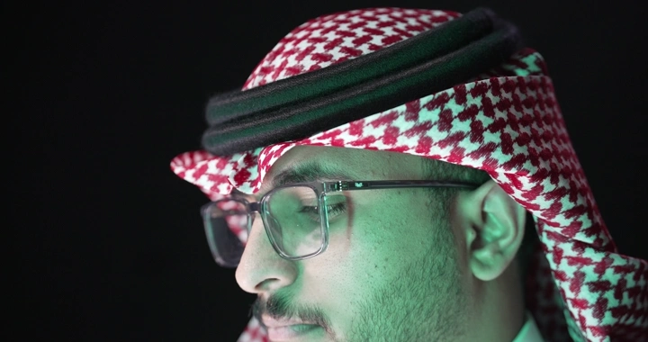 رجل يرتدي نظارات وعقال في إضاءة خافتة، لقطة قريبة.