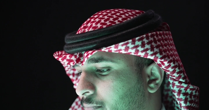 Man wearing red keffiyeh in dim lighting, close-up shot.