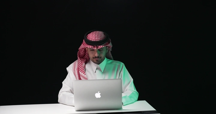 رجل سعودي يعمل على الكمبيوتر المحمول في استوديو مظلم، لقطة أمامية.