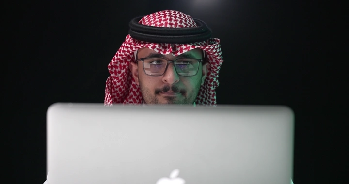 رجل سعودي يعمل على جهاز كمبيوتر محمول، لقطة أمامية.